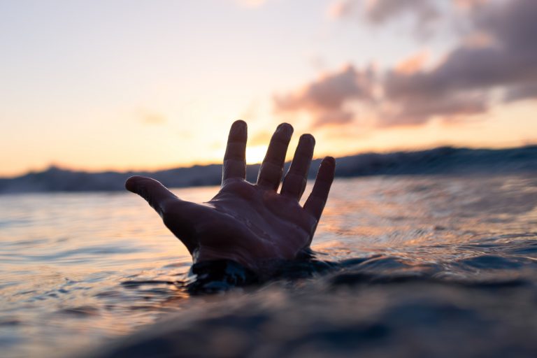 Hand of a drowning man in a sea at a sunset