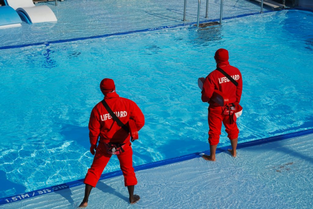 RLSS Swimming Pool Emergency Rescue Award Two men in red suits standing in front of a swimming pool