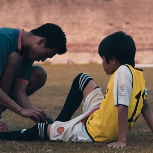 2 men in red and white jersey shirt sitting on ground during daytime